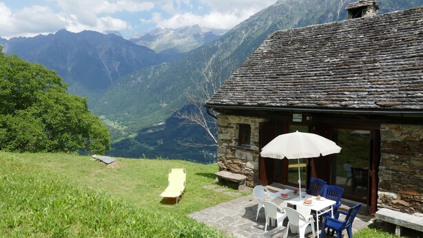 Un edificio de piedra con una mesa y sillas en el patio, una silla amarilla y una sombrilla blanca.