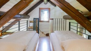 Un dormitorio acogedor en el ático, con techo inclinado, vigas de madera y una barandilla de metal, además de un ventanal.