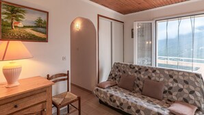 Un salon chaleureux avec un plafond en bois, un canapé agrémenté de coussins à motifs, une chaise en bois, un bureau avec une lampe et un tableau représentant un paysage.