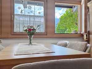 Un coin repas comprenant une table, des chaises, un vase avec des fleurs et une fenêtre donnant sur un paysage verdoyant.