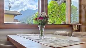 A room with a wooden table, a vase with flowers, and a view of mountains through a window.