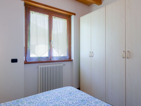A bedroom with a bed, a window with curtains, a radiator, and a wardrobe. - Azalea (GLA103) by Interhome (Gera Lario)