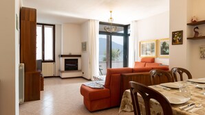 A living room with a fireplace, a sofa, a dining table set for two, and a balcony with a view. - Salice Verde (GLA134) by Interhome (Gera Lario)