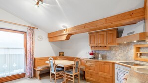 A kitchen with wooden cabinets, a dining table with chairs, a window with curtains, and a clock on the wall. - Prieslern by Interhome (Bramberg am Wildkogel)