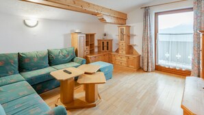 A cozy living room with a wooden ceiling, a sofa, a coffee table, and a window with curtains. - Prieslern by Interhome (Bramberg am Wildkogel)