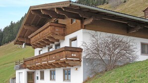A two-story chalet with a wooden balcony, a garage, and a view of a hillside. - Prieslern by Interhome (Bramberg am Wildkogel)