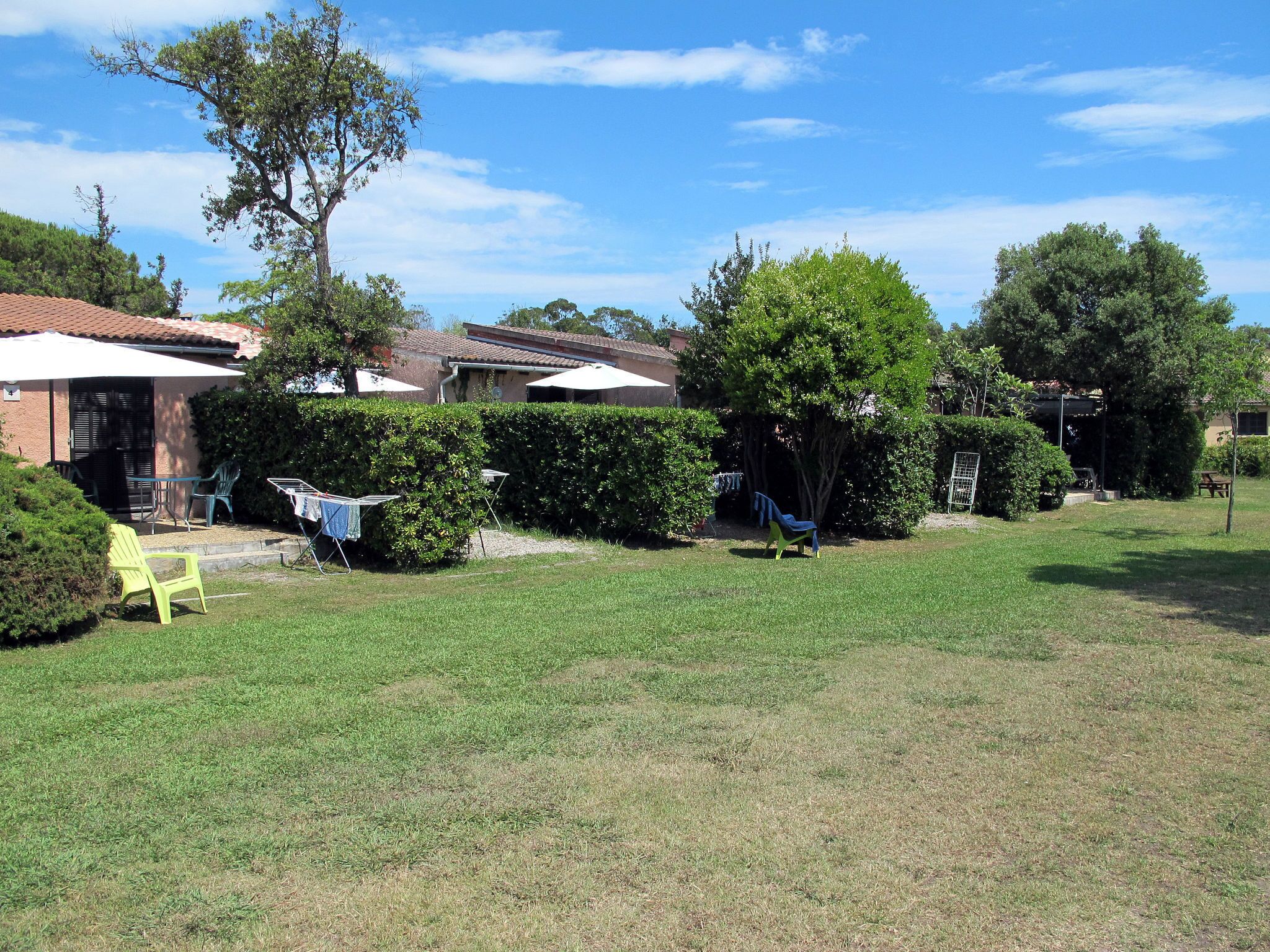 A residential backyard with a lawn, a patio area with chairs, and a house with a tiled roof.