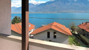 A view of a lake with mountains in the background, a wooden deck, and a building with a red roof.