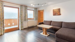 A modern living room with a brown sofa, a wooden coffee table, and a large window with curtains. - Prieslern by Interhome (Bramberg am Wildkogel)