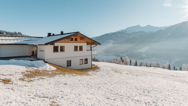 Un bâtiment à deux étages, doté d’un toit en pente, situé sur une pente enneigée et offrant une vue sur les montagnes en arrière-plan.