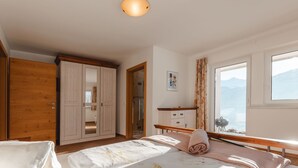 Une chambre avec deux lits, une armoire en bois, une salle de bain et une grande fenêtre donnant sur la montagne.