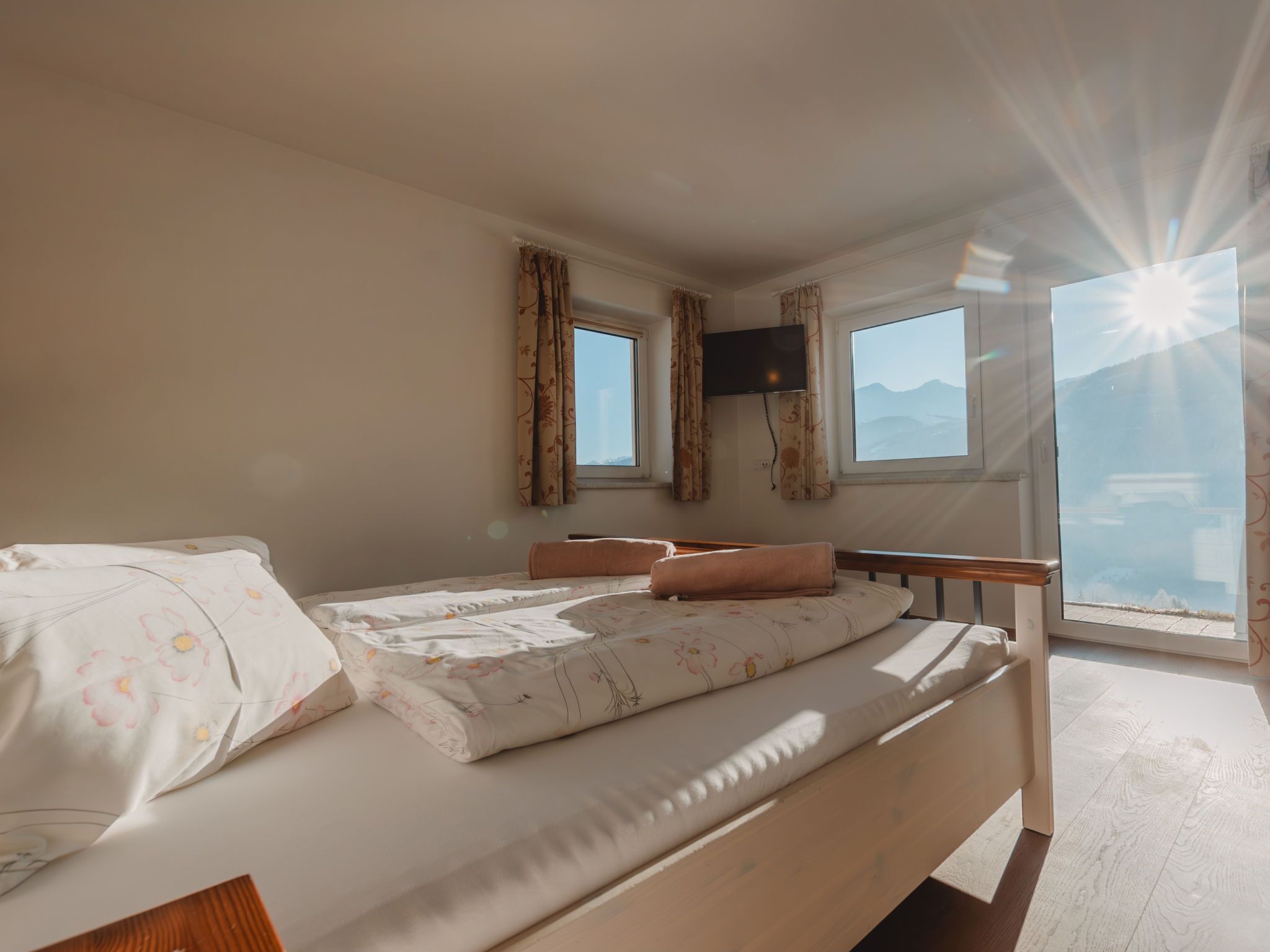 A bedroom with a bed, two windows, a TV, and a view of the mountains.