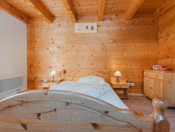 Ein Schlafzimmer in einer Holzhütte mit einem Bett, zwei Nachttischen mit Lampen, einem Holzschrank und einem Wandbild.