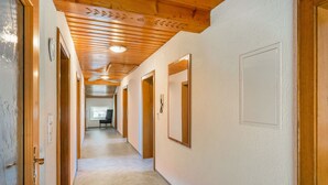 A hallway with wooden ceilings and doors, carpeted floors, and a view into another room. - Weberbauer by Interhome (Mittersill)