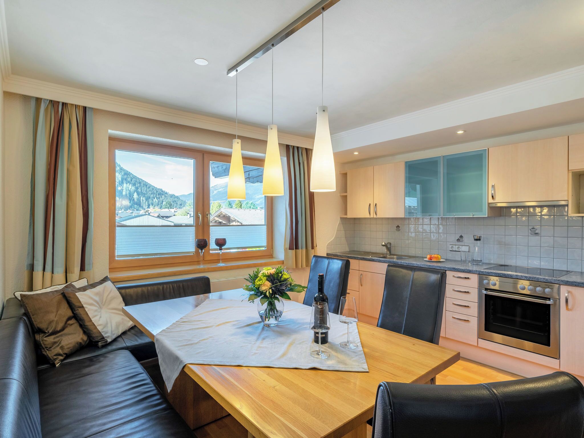 A modern kitchen with a dining area, featuring a wooden table, black leather seating, and a view of a lake through large windows.