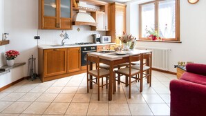 Una cocina con armarios de madera, una mesa de comedor con sillas, una estufa y un ventanal con flores.