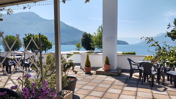 An outdoor terrace with tables and chairs, potted plants, and a view of the sea and mountains. - Apartment Betti by Interhome (Domaso)