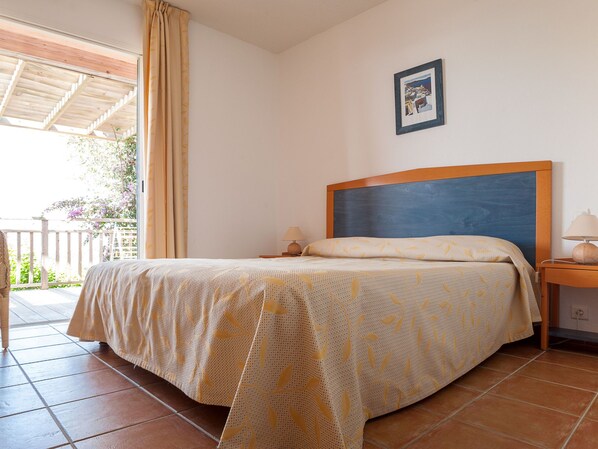 A bedroom with a bed, nightstands, a window with curtains, and a framed picture on the wall.