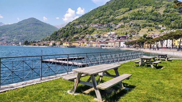 A lakeside view with a wooden dock, picnic tables, and a metal railing.