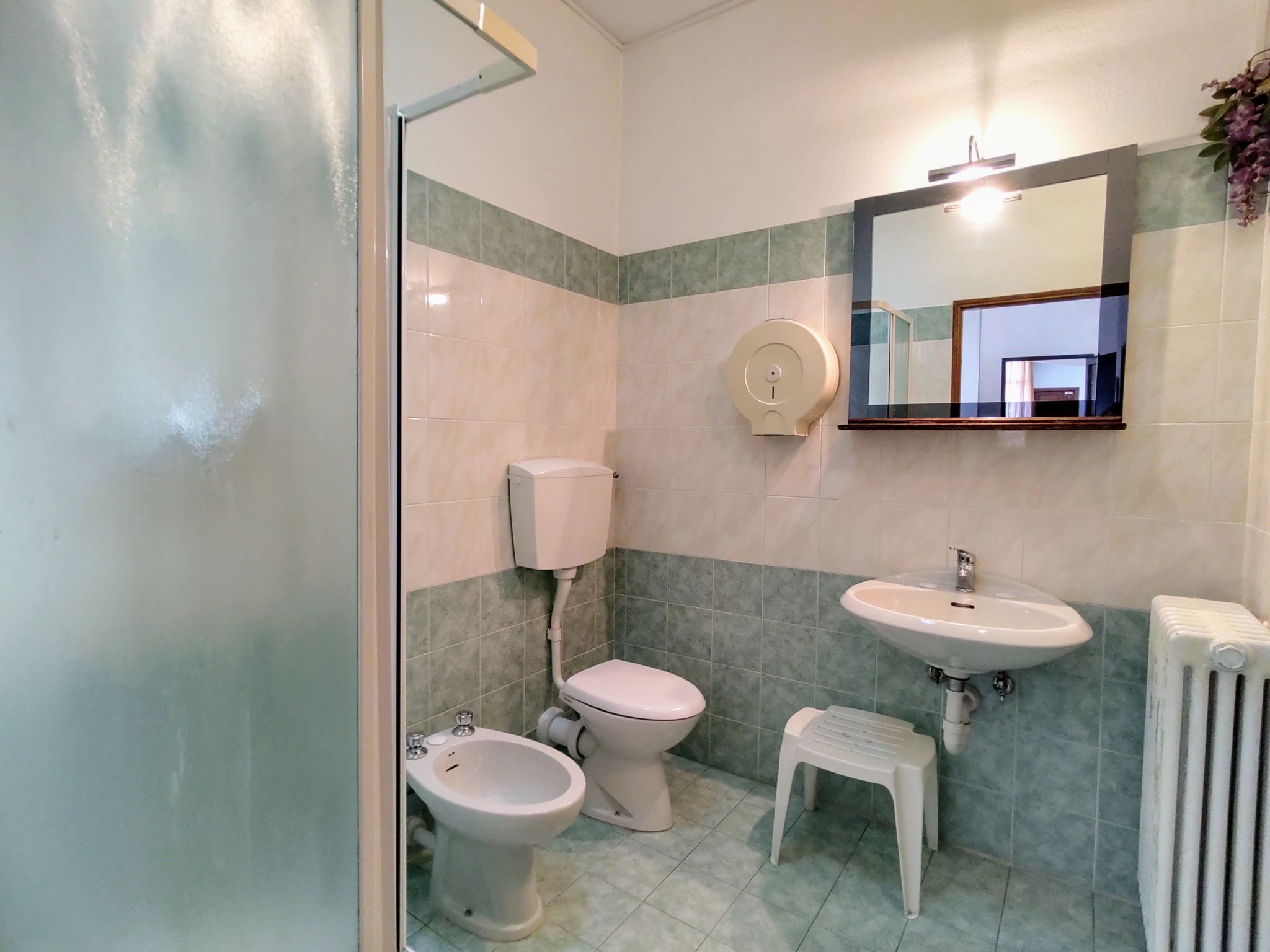 Et badeværelse med toilet, bidet og vask, en lille skammel samt en håndtørrer.