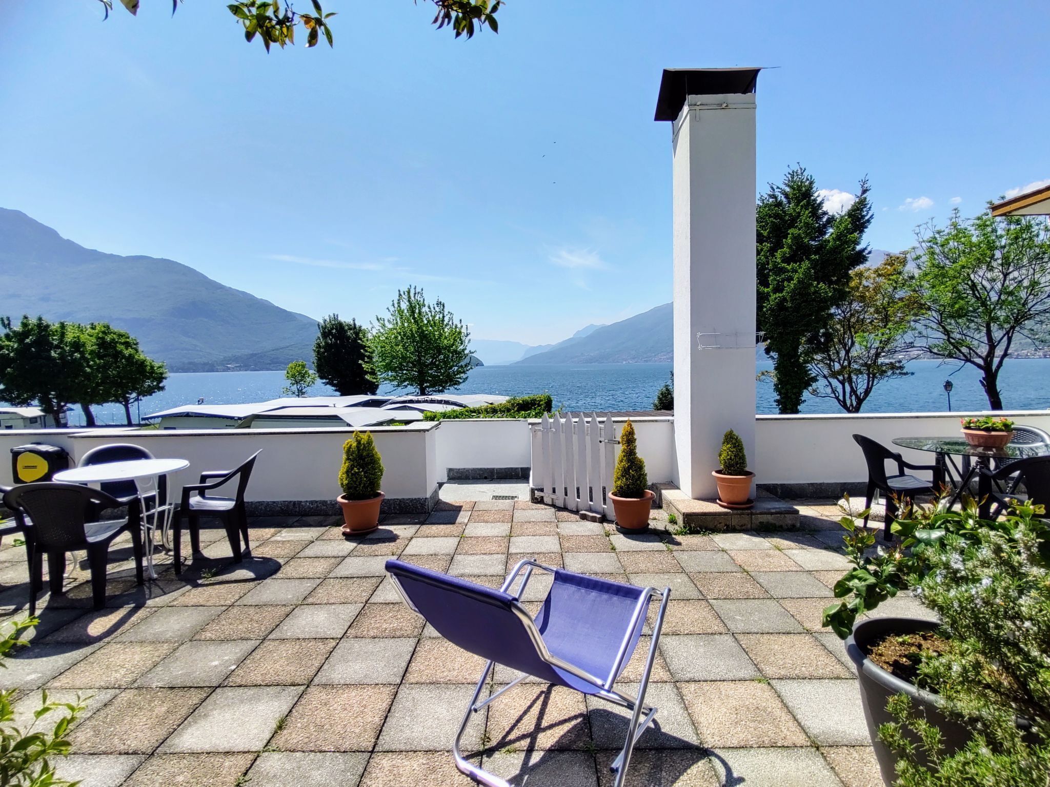 Eine Terrasse mit Blick auf einen See und Berge, mit Sitzmöbeln im Freien und Kübelpflanzen.