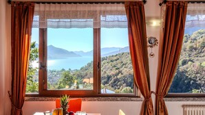 Una mesa de comedor con alimentos para el desayuno, una vista de un lago y montañas a través de una ventana, y cortinas.