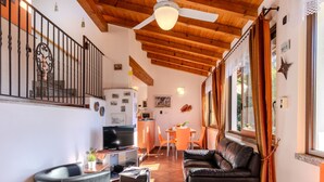 Amplia sala de estar con techo de madera, un sofá de cuero negro, una mesa de comedor con sillas naranja y una cocina al fondo.