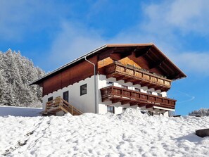 A chalet with a wooden balcony, a wooden staircase, and a snowy landscape.