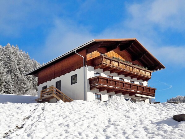 A chalet with a wooden balcony, a wooden staircase, and a snowy landscape.