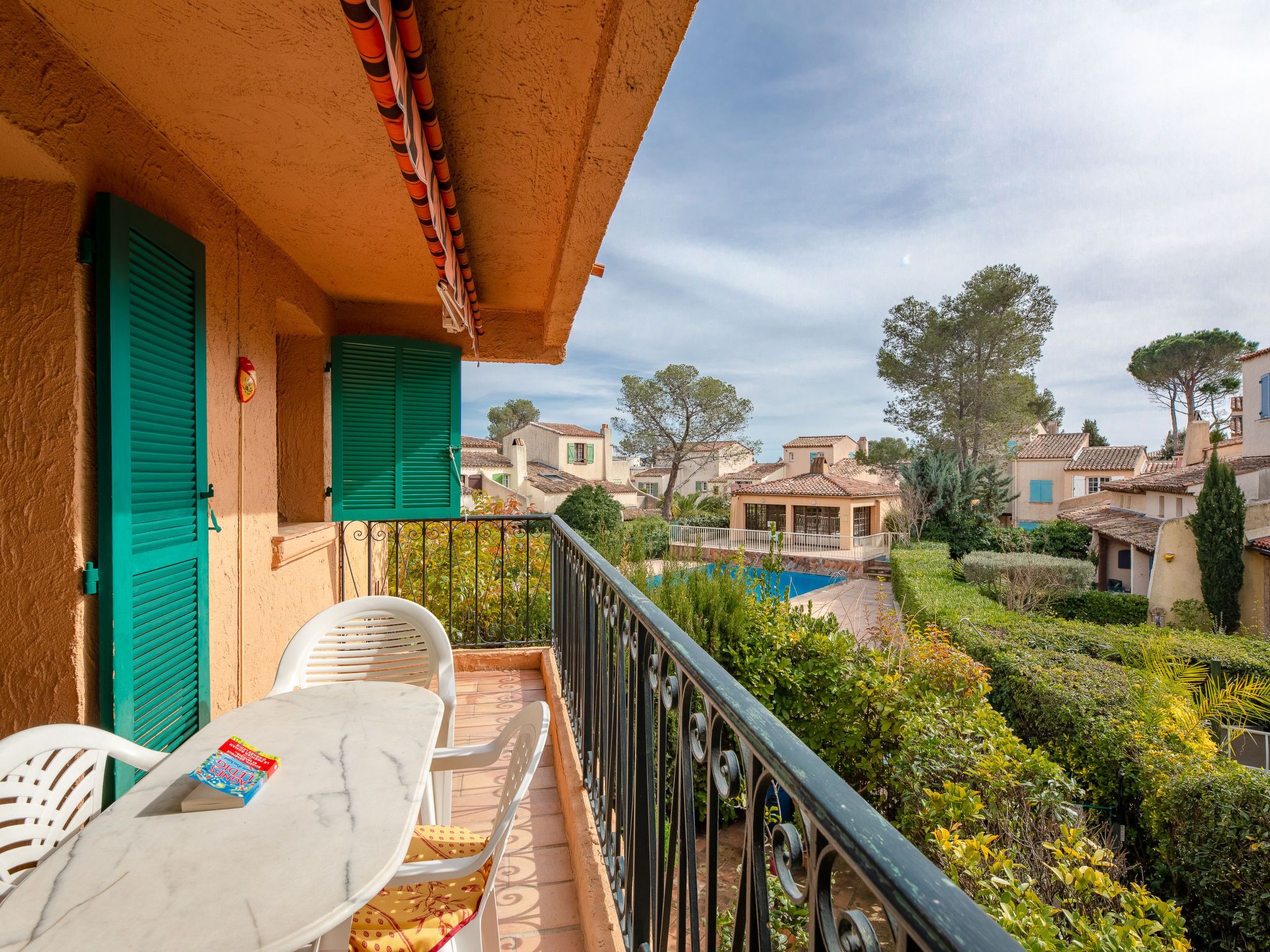 A balcony with a table and chairs, a book, and a view of a swimming pool and surrounding buildings.