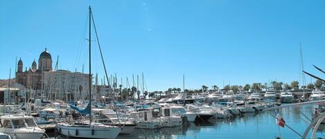 A marina with numerous boats docked, a wooden pier, and a large building with domed architecture in the background.