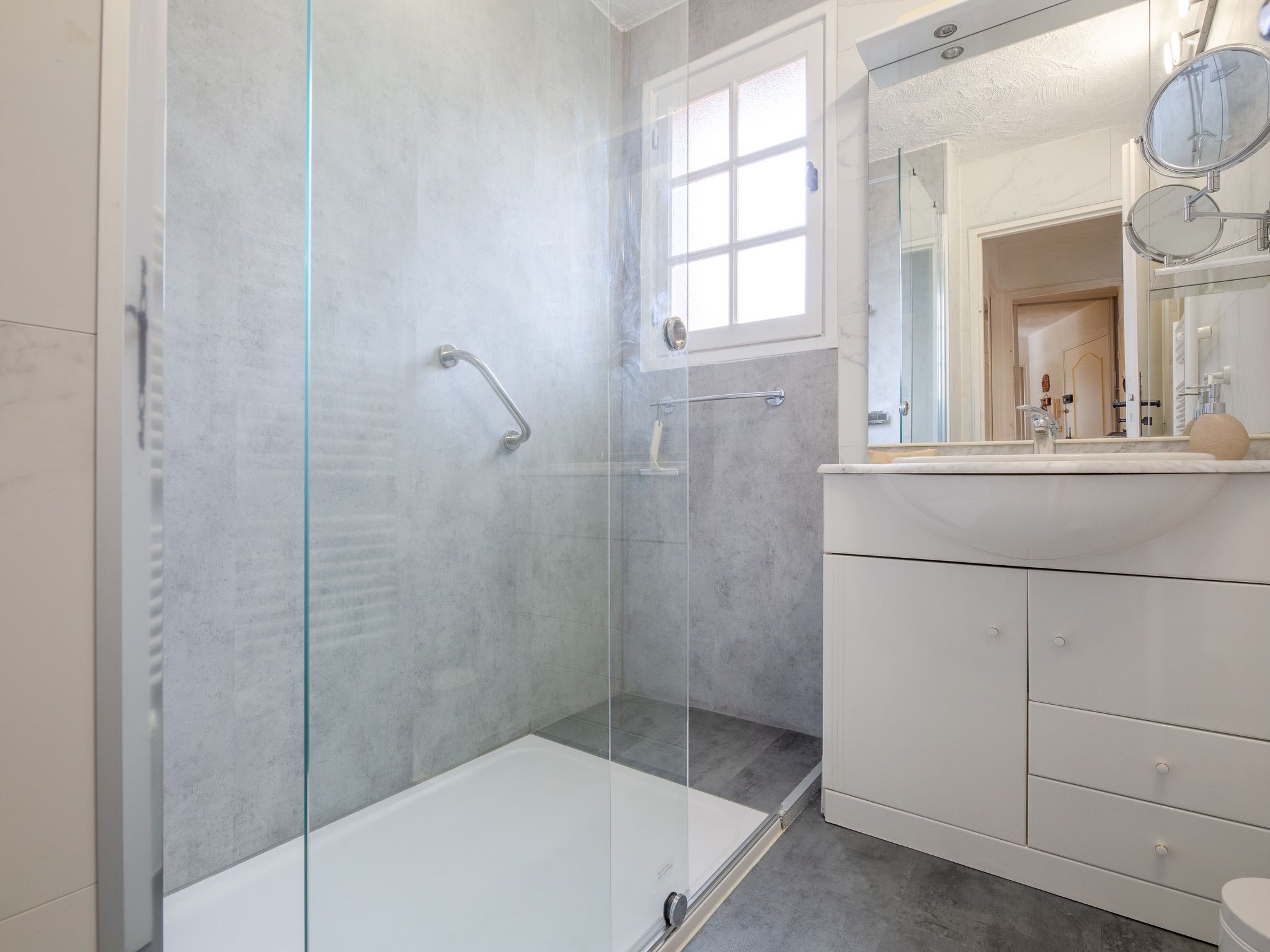 A modern bathroom with a glass shower enclosure, a white bathtub, and a vanity with a mirror and sink.