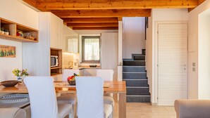 A modern kitchen with wooden beams, a dining area with white chairs, and a staircase leading to another level. - Marcello by Interhome (Gravedona)