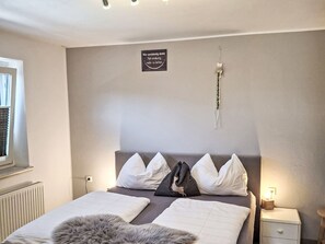 A bedroom with a bed, a bedside table, a nightstand, a window with blinds, and a wall-mounted sign. - Tobias 1 by Interhome (Radstadt)