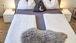 Een keurig opgemaakt bed met witte lakens, een zachte grijze plaid, en twee nachtkastjes met lampen.