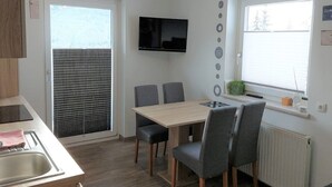 Een kleine keuken met een eethoek, een aan de muur bevestigde televisie en een raam met luxaflex.