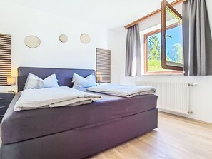 Un dormitorio moderno con una cama grande, una mesita de noche, una ventana con cortinas y un radiador.