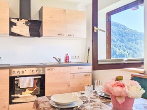 Una cocina con armarios de madera, horno empotrado, ventana con vistas a la montaña y una mesa de comedor con platos y vasos.