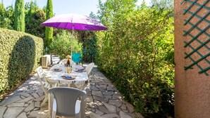 Eine Terrasse im Freien mit Esstisch, umgeben von Grünpflanzen und einem gepflasterten Weg.