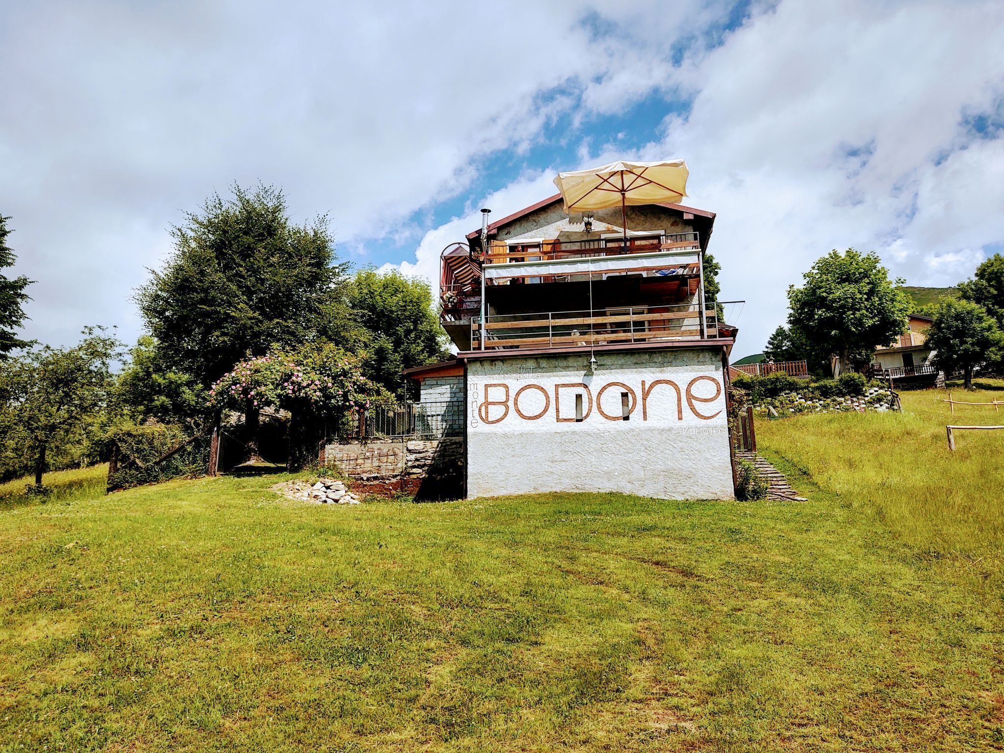 Un edificio con el nombre 'Bodone' en su fachada, rodeado de follaje y árboles.
