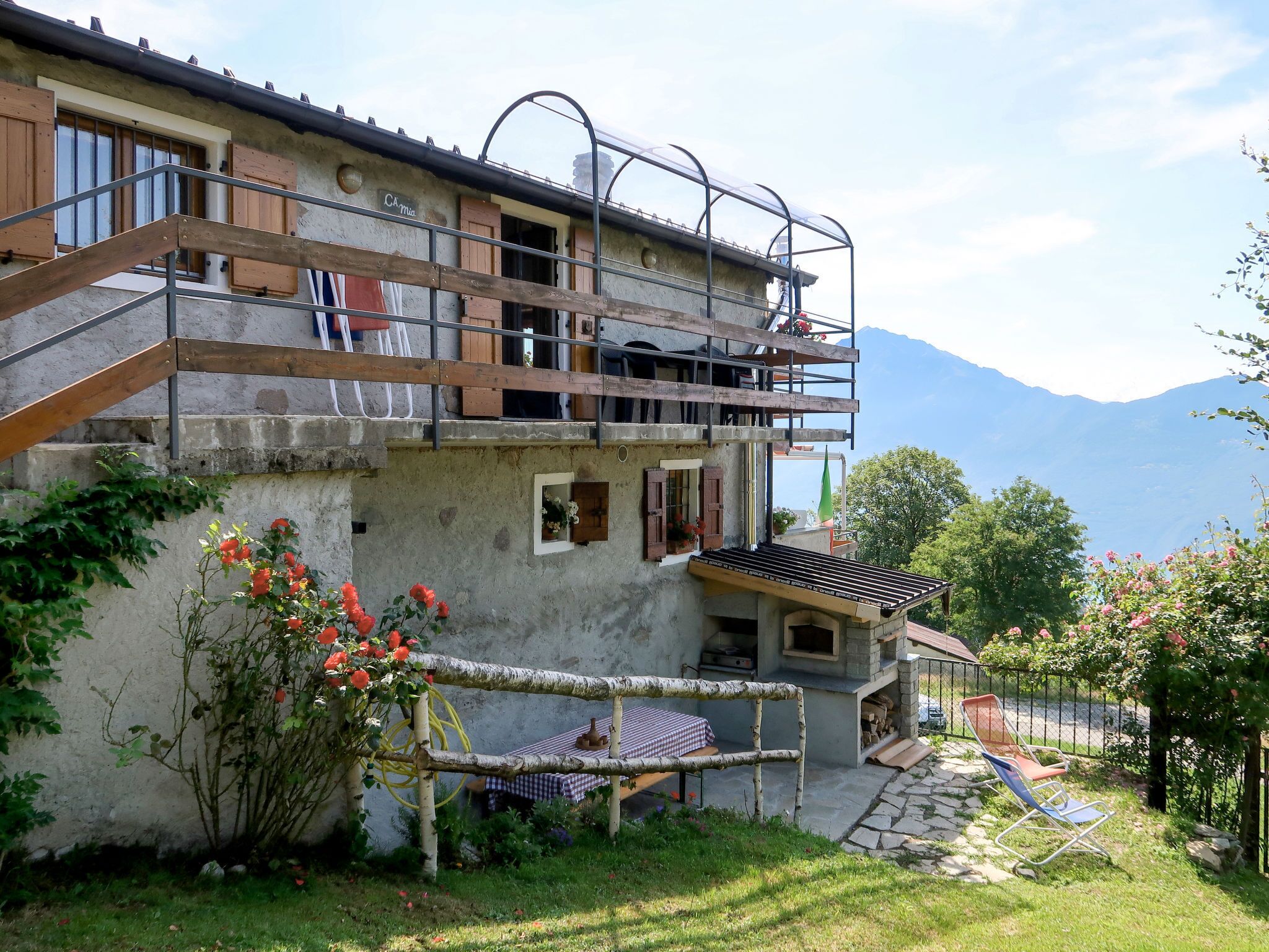 Un edificio rústico con un balcón, un pequeño jardín de rosas y vistas a montañas.