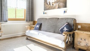 Ein gemütliches Zimmer mit Holzbalkendecke, einem grauen Sofa mit dekorativen Kissen, einem Nachttisch aus Holz und einer Heizung.