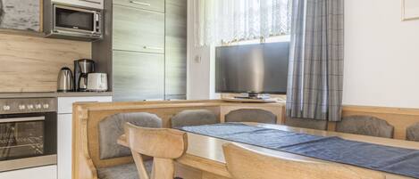 A modern kitchen with a dining area, wooden furniture, a microwave, a coffee maker, and a television.