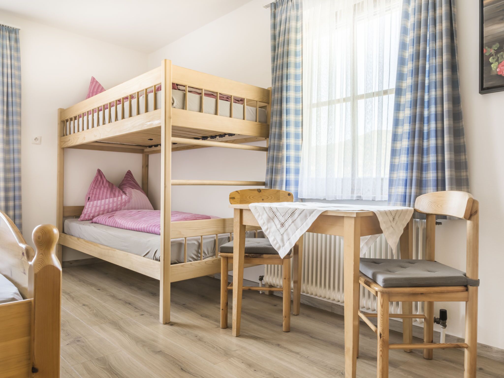 A bunk bed room with a table and chairs, a radiator, and plaid curtains.