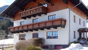 Ein mehrstöckiges Holzhaus mit Balkonen und großen Fenstern, umgeben von Schnee und Bergen.