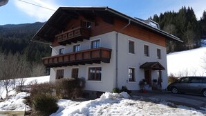 Eine zweistöckige Chalet mit Holzbalkon, geneigtem Dach und Blick auf einen verschneiten Berg.