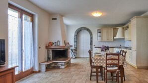 Een ruime woonkamer met een open haard, een eettafel met stoelen en een keuken met kasten.