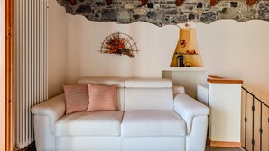 A cozy living room with a white sofa, a decorative wall piece, and a stone wall. - Pieve (GRV102) by Interhome (Gravedona)