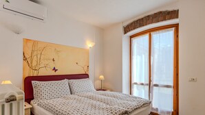 A neatly made bed with a patterned bedspread, a red headboard, and a wall-mounted air conditioner. - Pieve (GRV102) by Interhome (Gravedona)