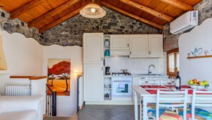 A cozy kitchen with white cabinets, a dining table with chairs, and a stone wall. - Pieve (GRV102) by Interhome (Gravedona)